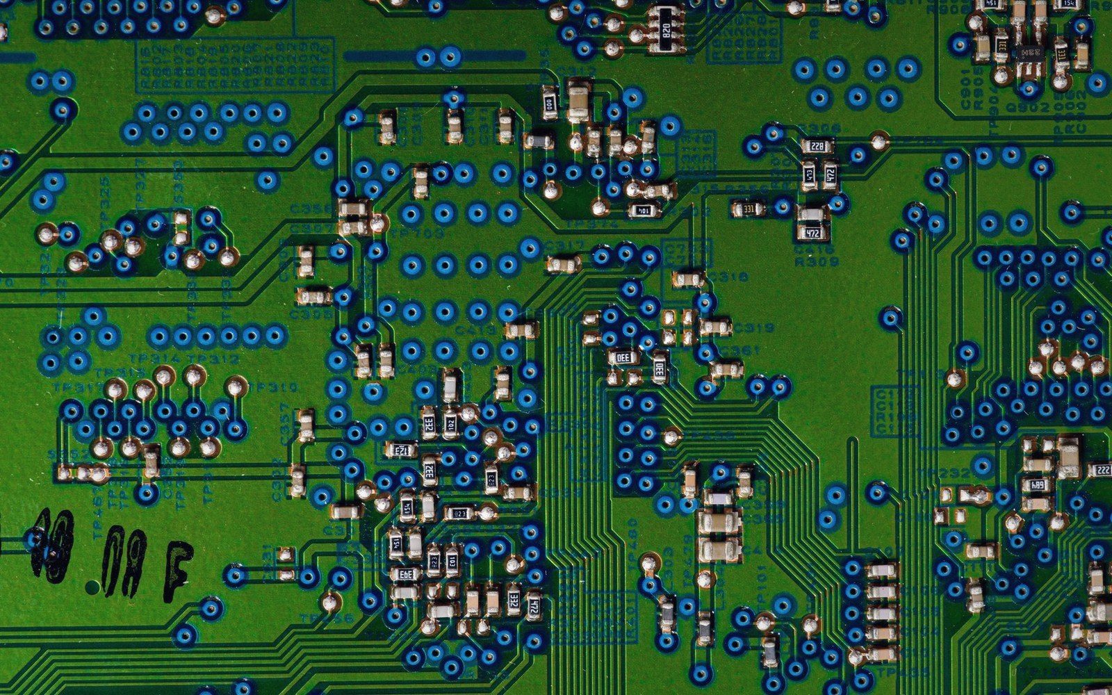 Close-up of a green circuit board with soldered components and blue-ringed via holes